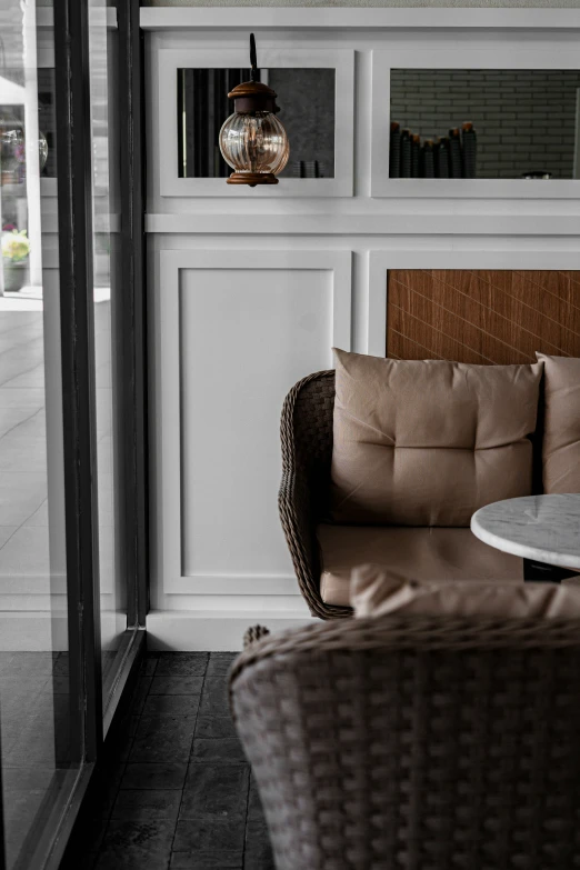 an outdoor seating area, including the arm of a wicker chair, with two side tables on one side and a table with glass top on another side of the other