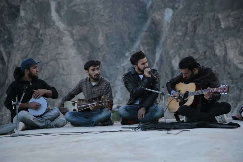 the five men are sitting on a ledge with acoustic instruments