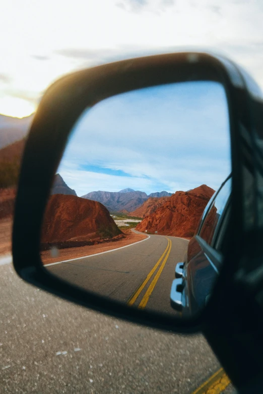 a view through a rear view mirror of a car driving along the side of a mountain