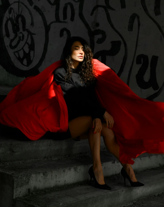 a woman sitting on the step wearing a red cape
