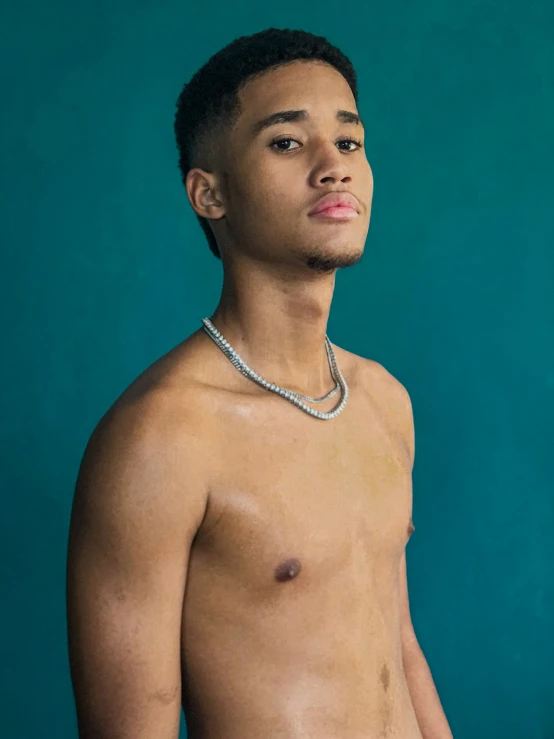 a young man without a shirt standing next to a green wall
