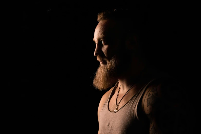 a man with a beard and necklace standing in the dark