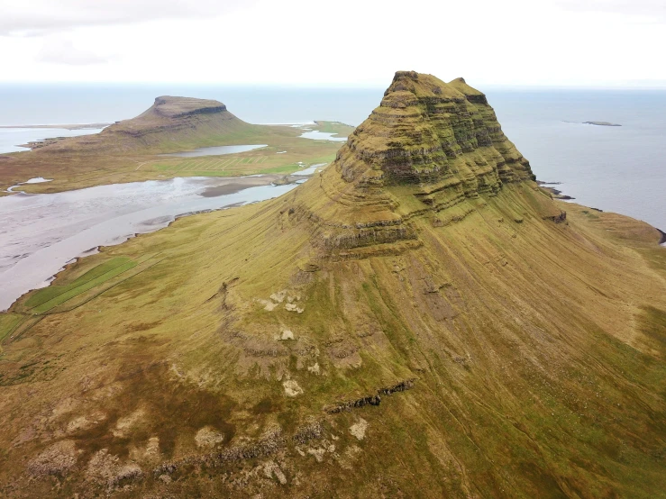 an aerial view of a small hill with water in the distance