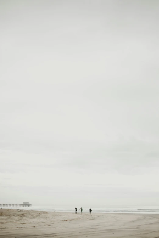 people walking along the beach in the distance with a kite in the sky