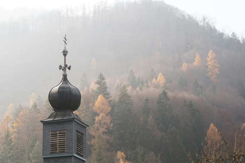 an old tower with a weather vane stands on the edge of a tree covered hillside