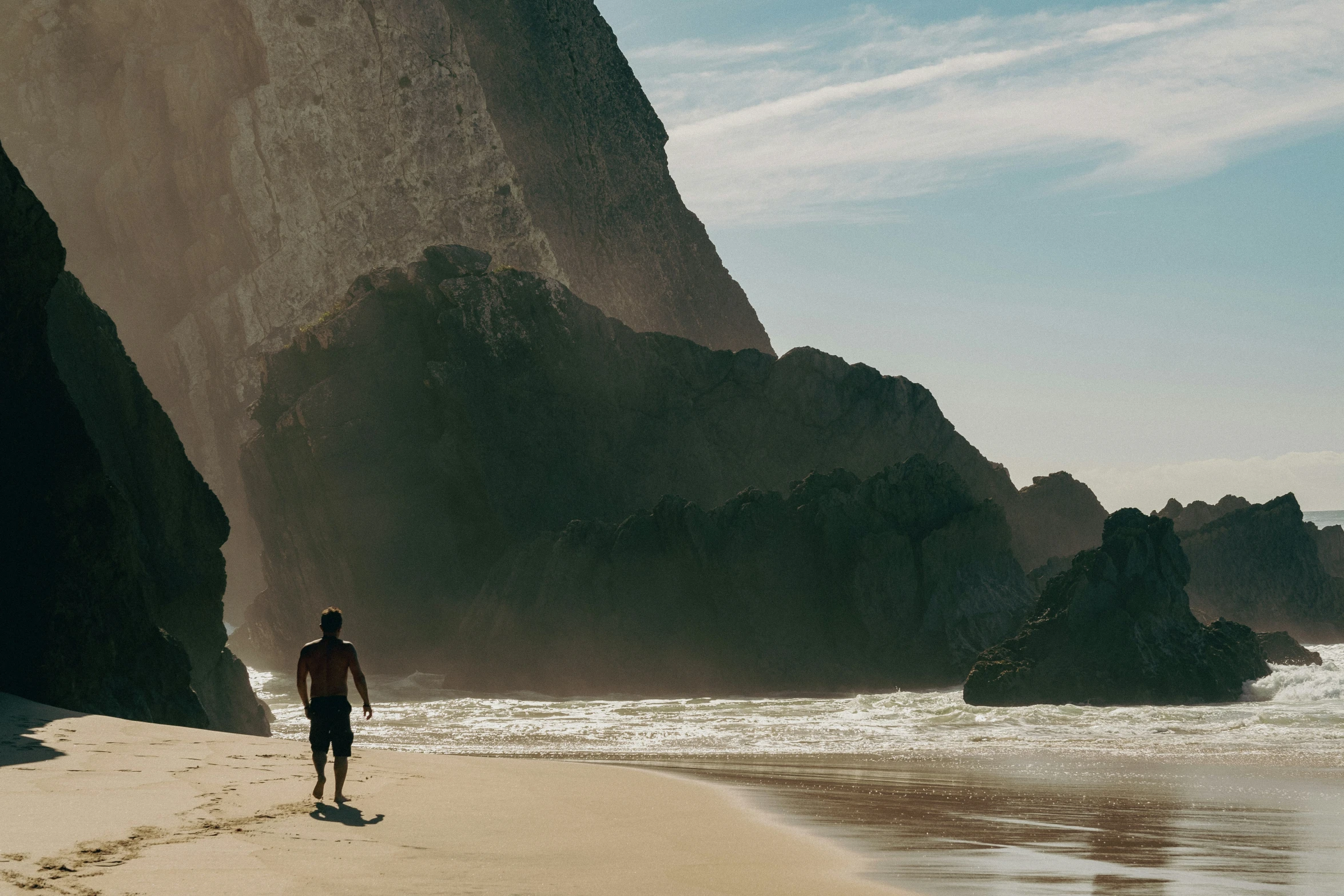 person walking on the beach towards a large cliff