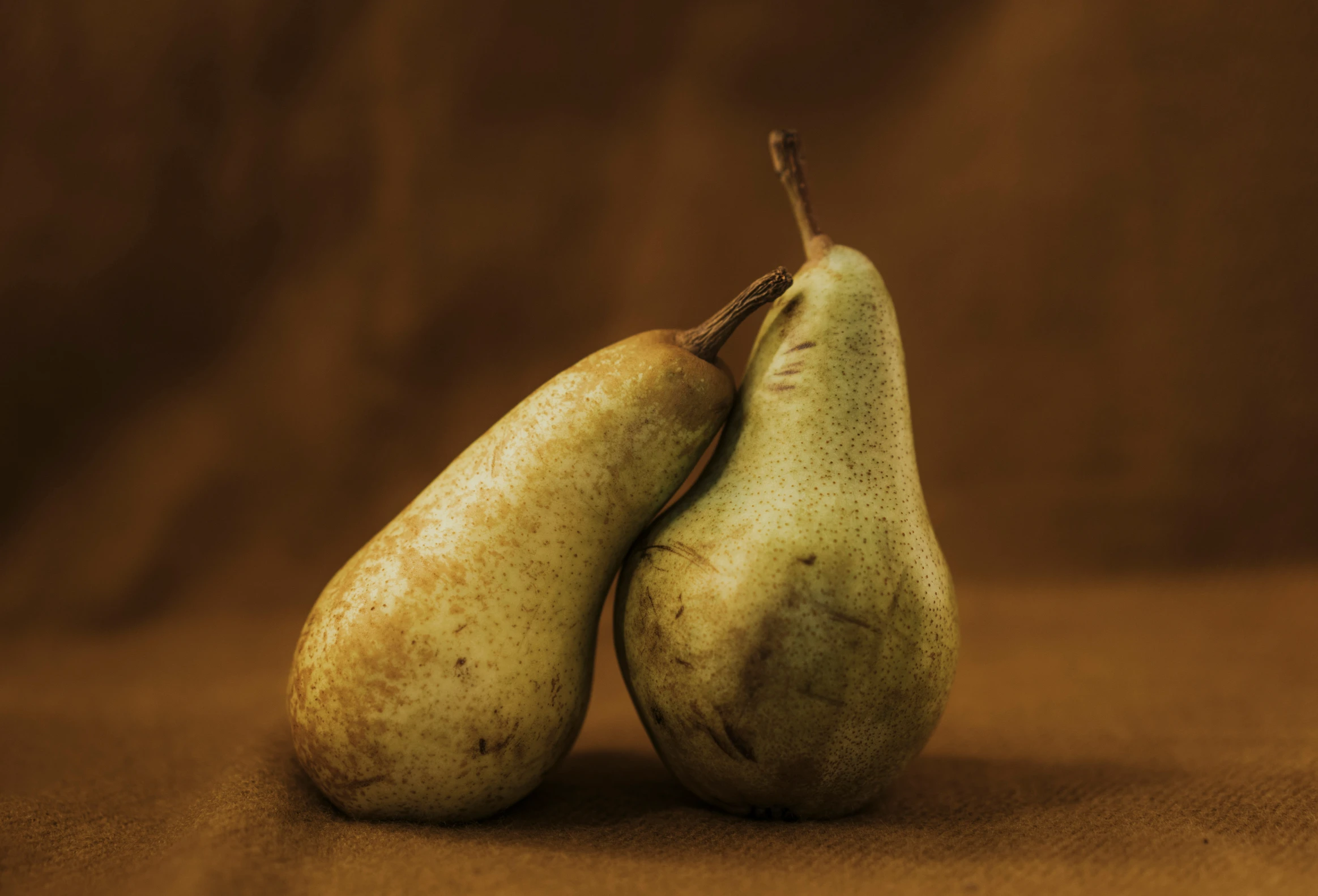 two pears sitting side by side on a brown background