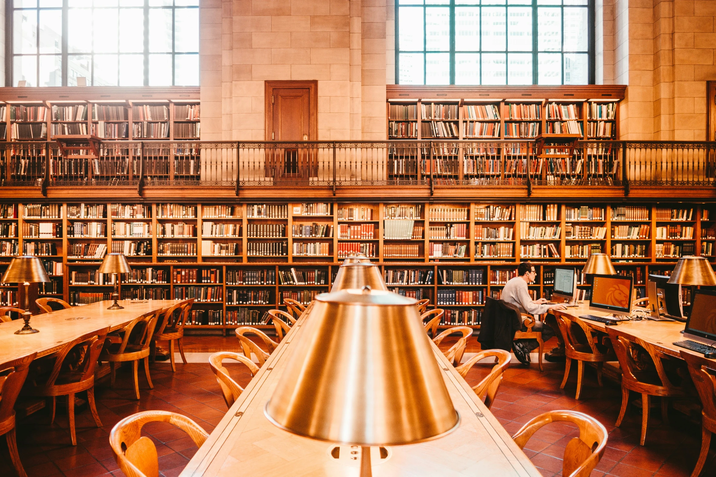 people sitting at long tables in a public liry with bookshelves