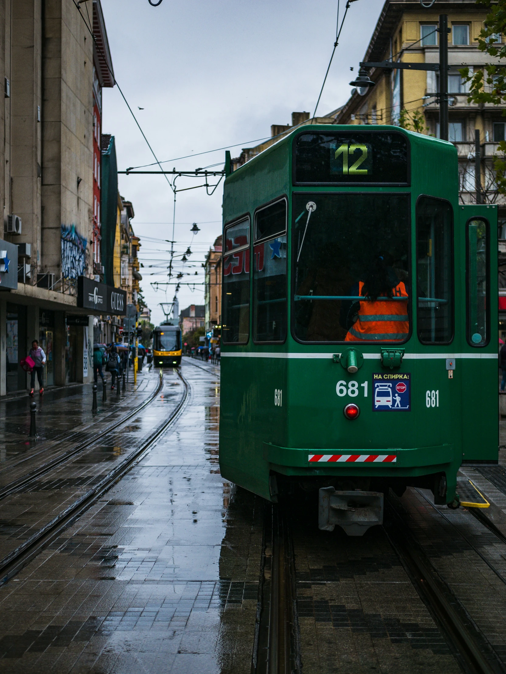 people are walking near a green trolley on a rainy day