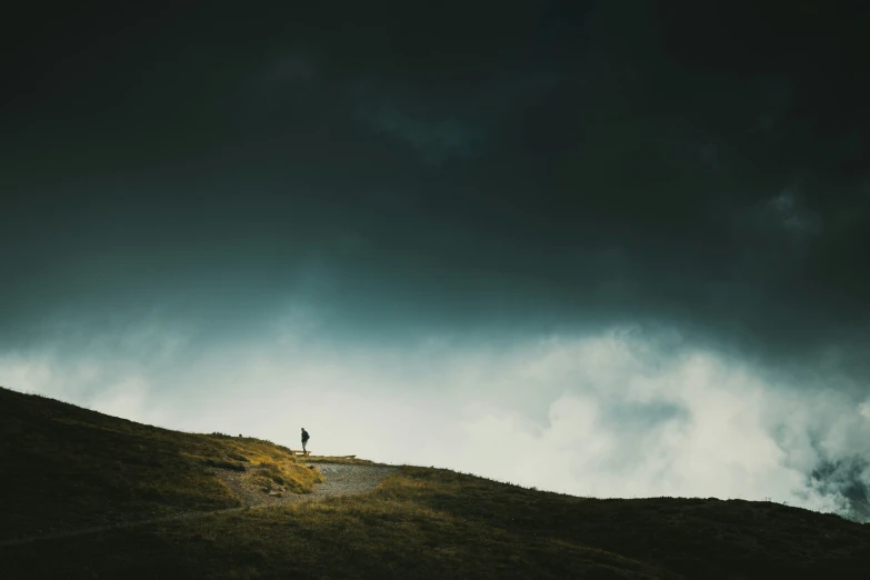 a person standing on top of a hill with a storm sky behind them