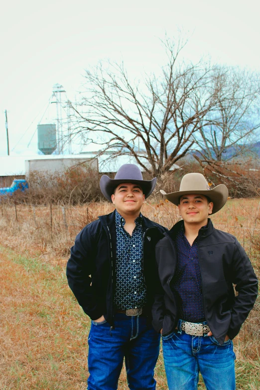 two young men standing in a field, one wearing a cowboy hat