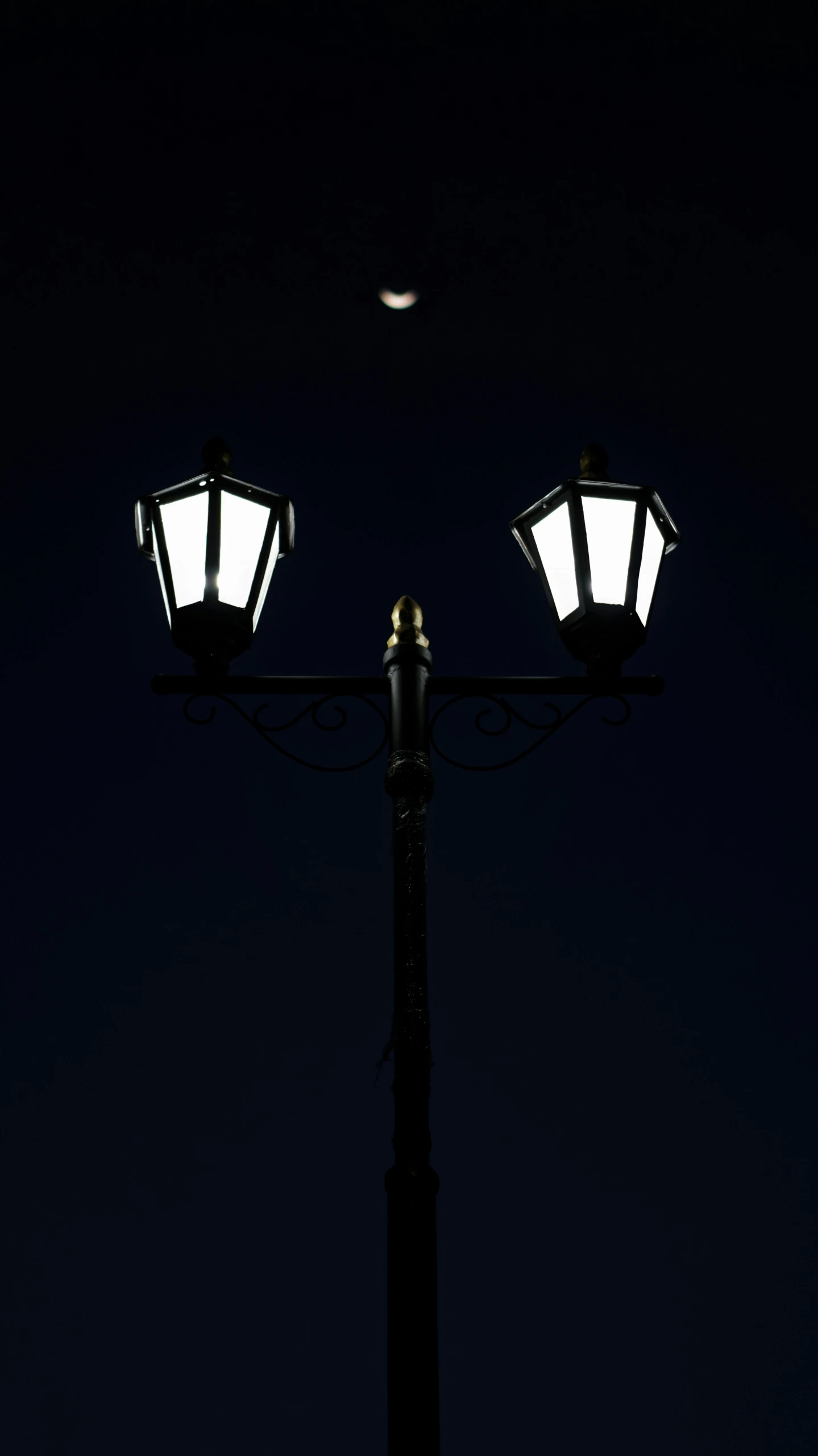 a street light on a pole at night with a moon in the distance