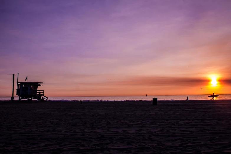 the sun sets in the background and there is a lifeguard tower in the foreground