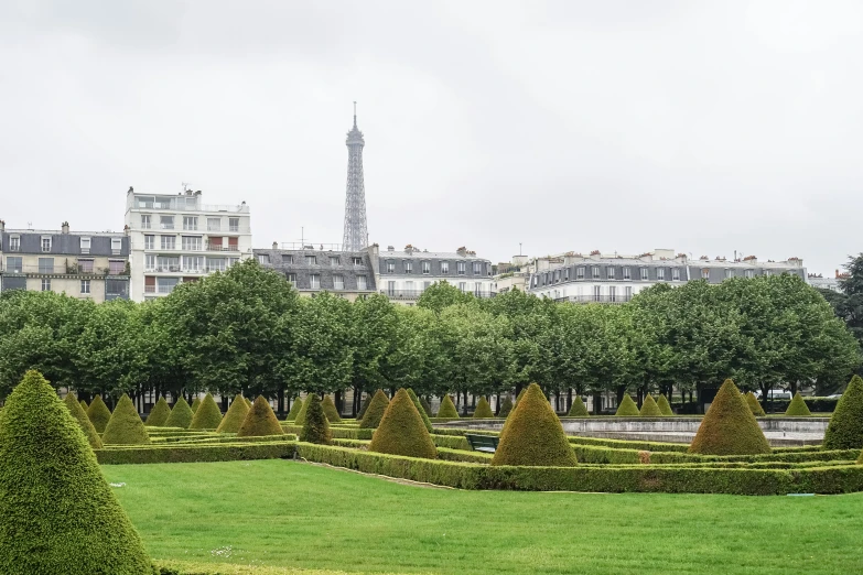 there is a building in the distance behind many trimmed bushes