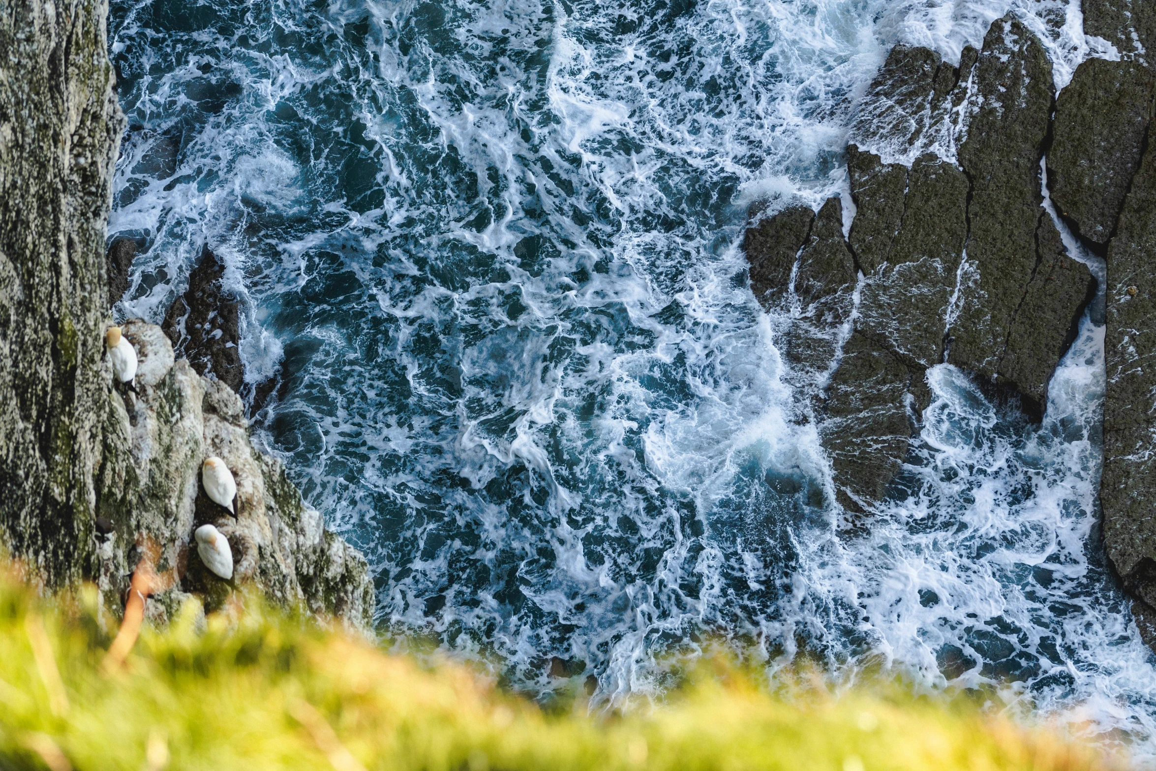 an aerial view of the ocean and cliffs with rocks in front