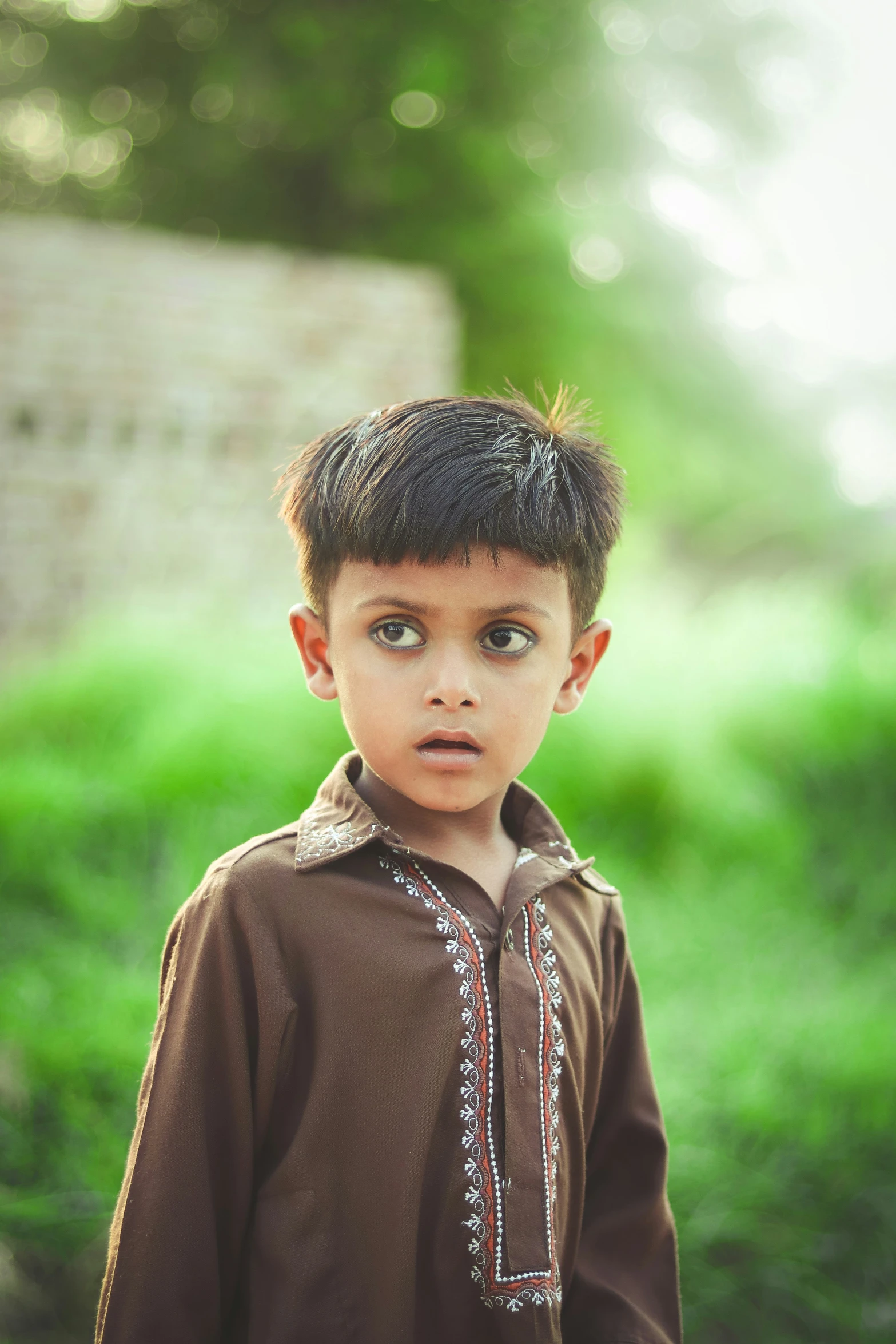 a boy wearing a brown shirt is standing in grass