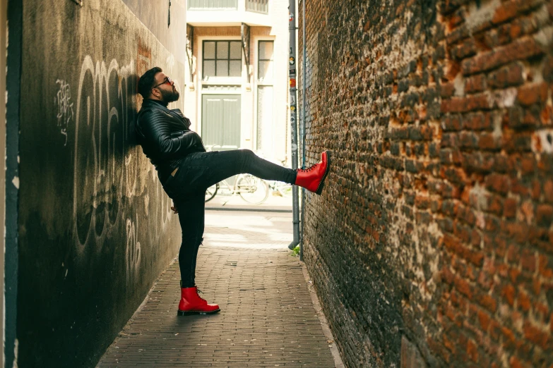 a man with a long beard and red shoes is leaning against a brick wall