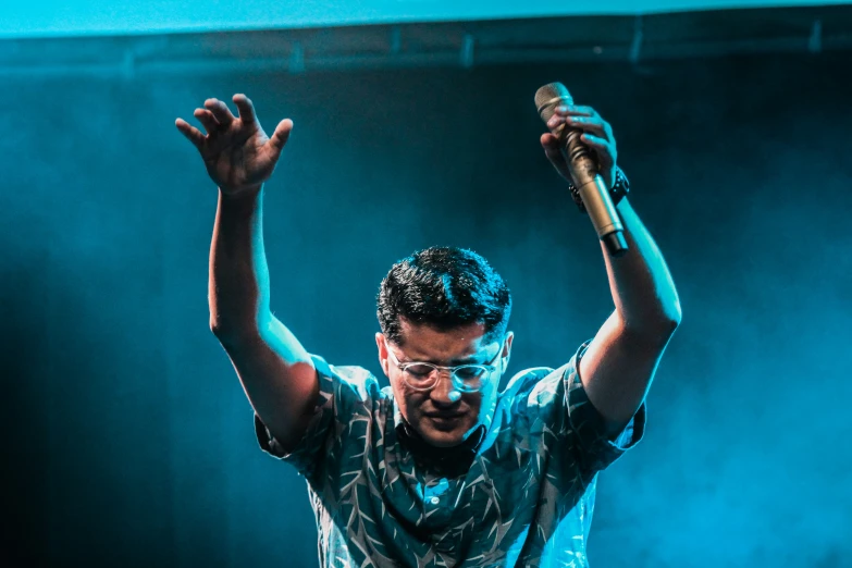 man singing into microphone while holding his arms up