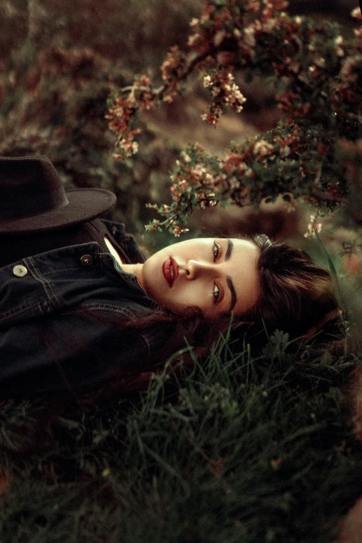 a girl with a hat on lays in grass