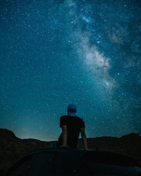 a person sitting on top of a car under the night sky