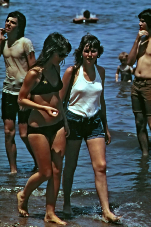 two women in swim suits standing in shallow water at a beach