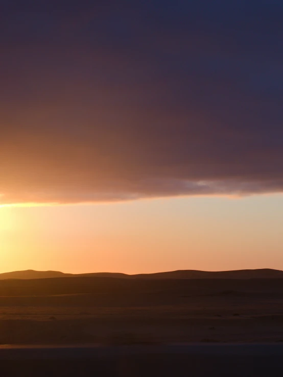 the setting sun behind a cloudy, silhouetted beach dune