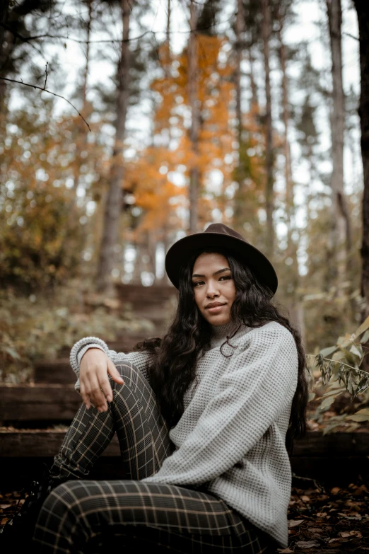 a woman wearing a hat is sitting in the woods