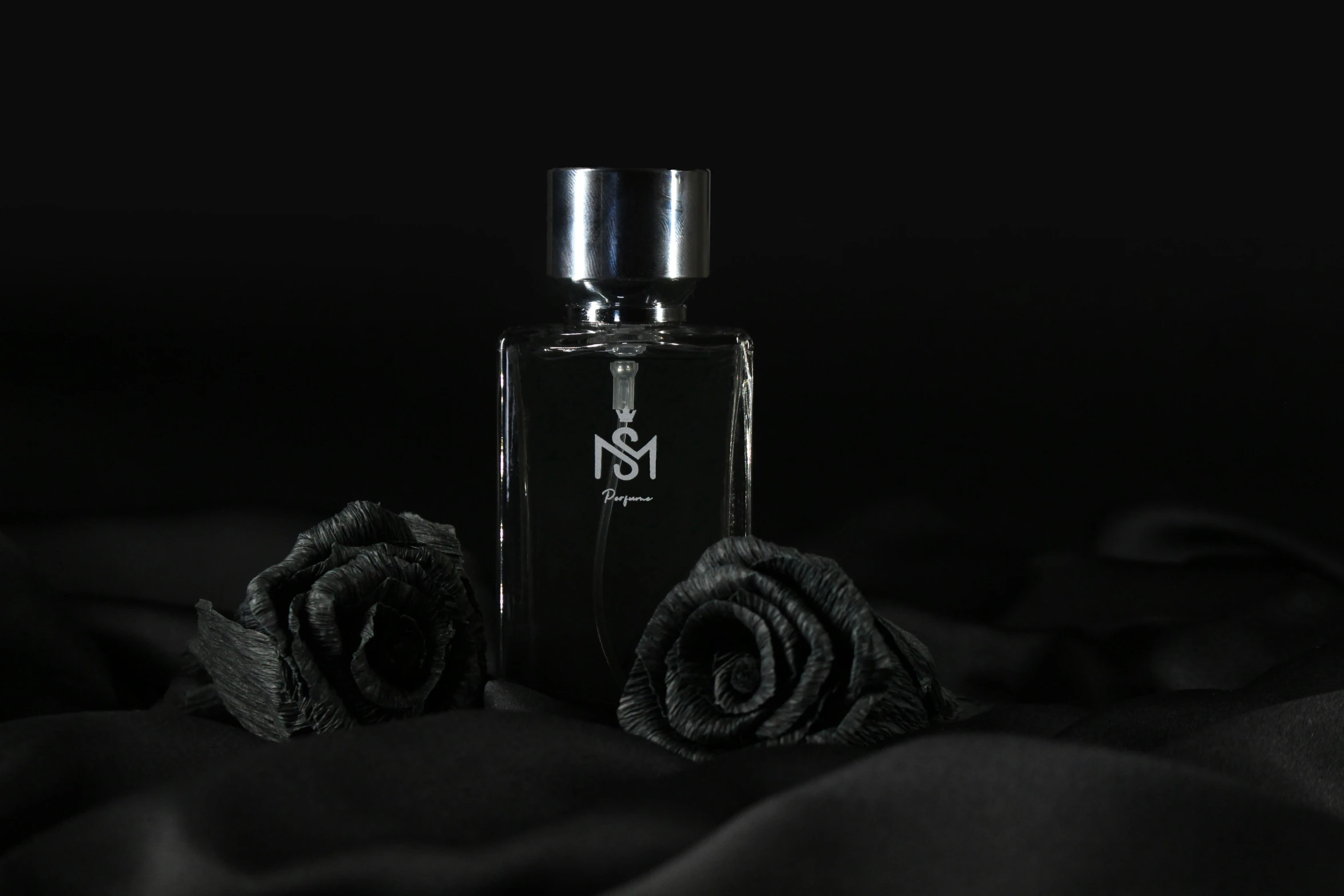 an elegant bottle with rose petals sits upon black cloth