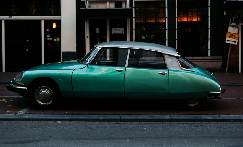 an old green sports car parked on the side of the street