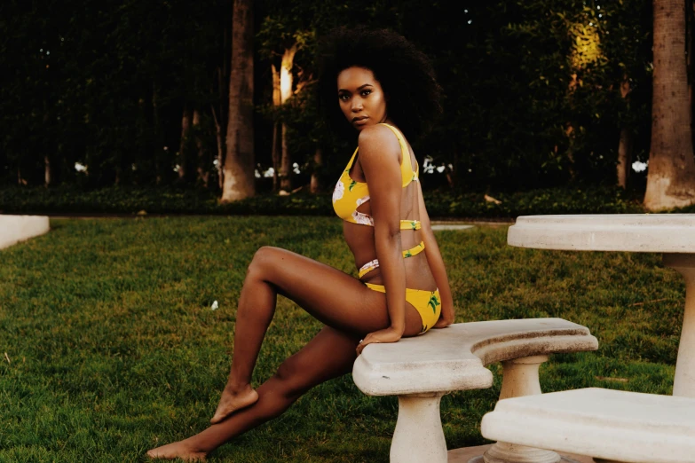 a young black woman wearing a yellow bathing suit and sitting on a park bench