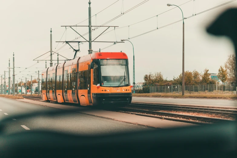 an orange passenger train moving on tracks in a city