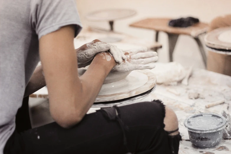 a man standing in front of a potters wheel holding soing with his hand