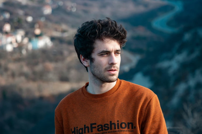 a male model with dark curly hair looks down on the mountain