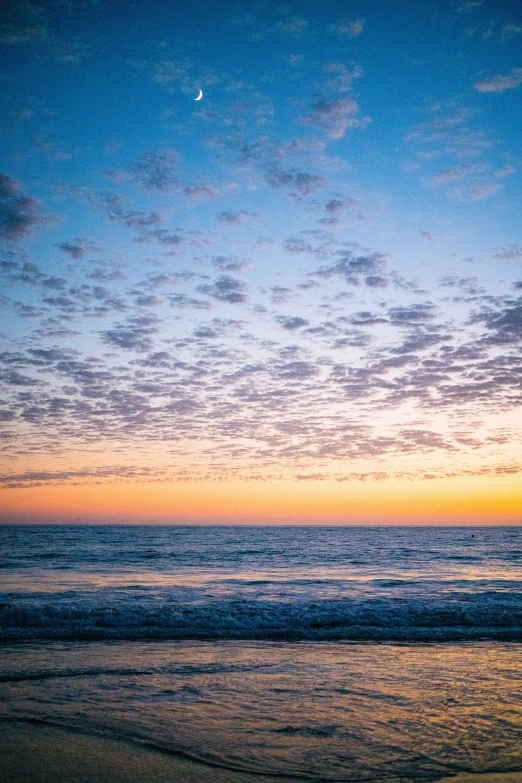 sunset with clouds over water and a surfboard in the foreground