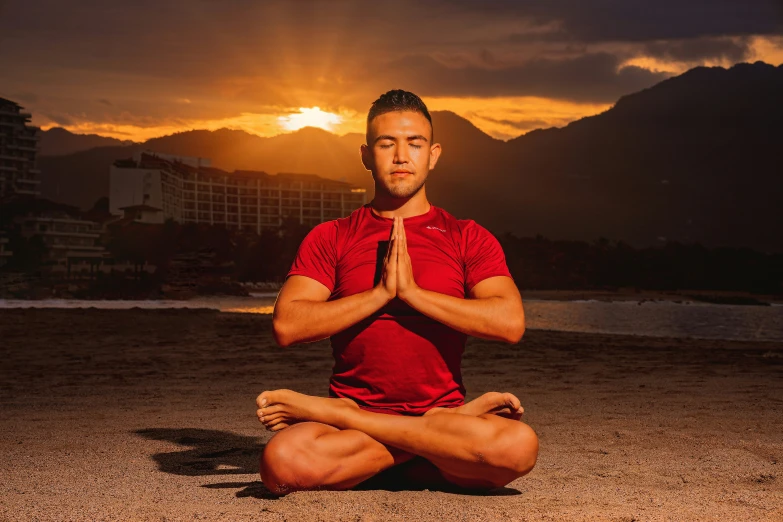 a man is sitting in a yoga position while wearing a red shirt and shorts