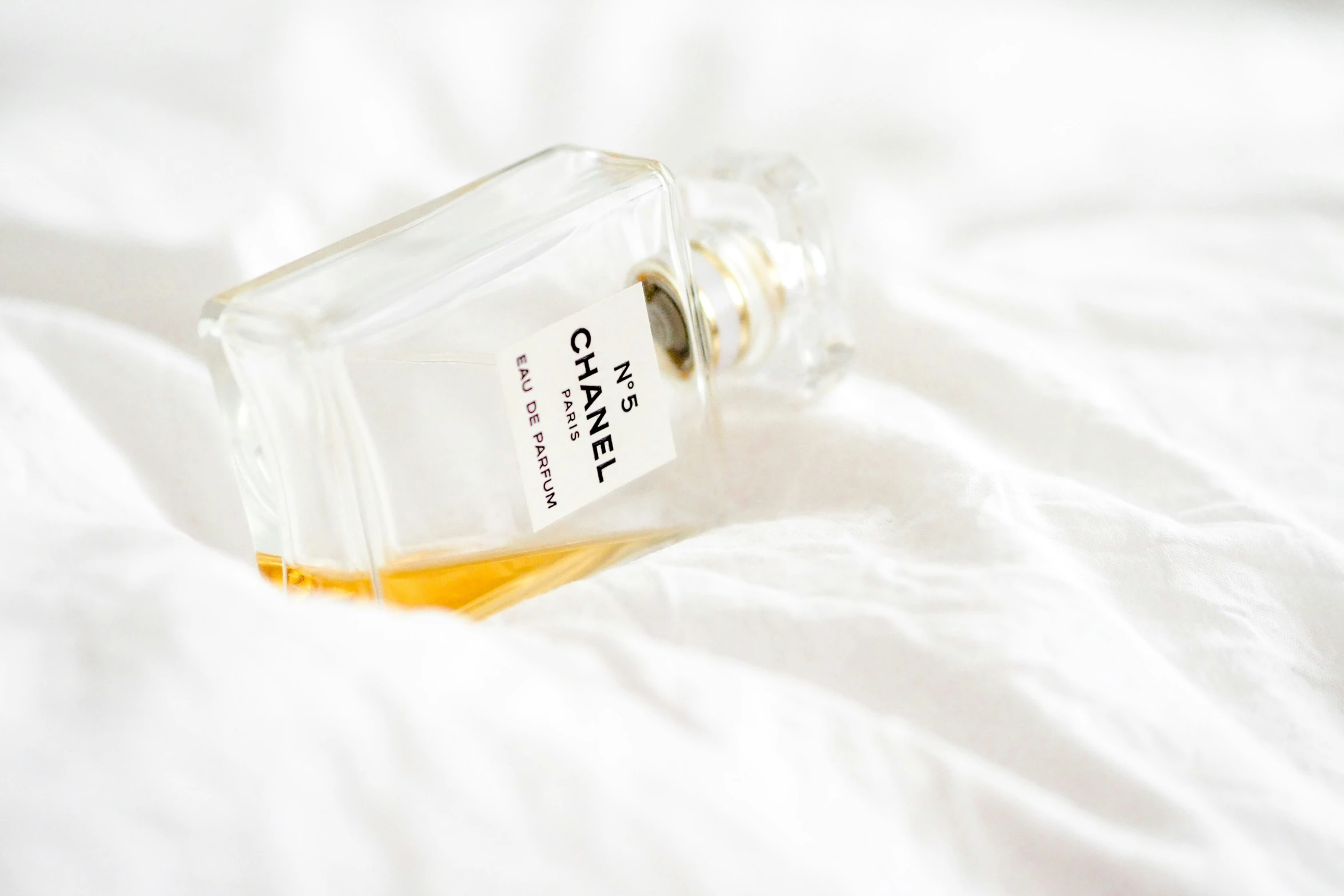 an empty bottle of cologne on a white bed sheet