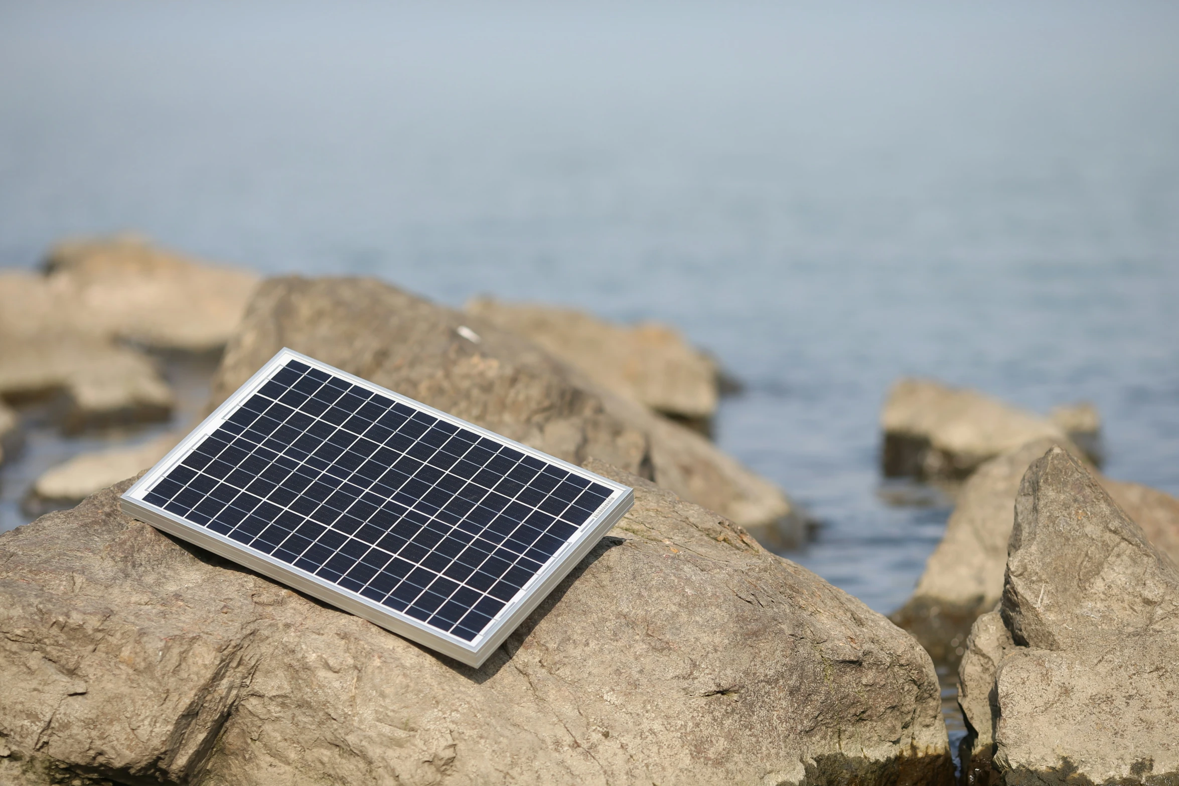 a solar panel laying on some rocks by water