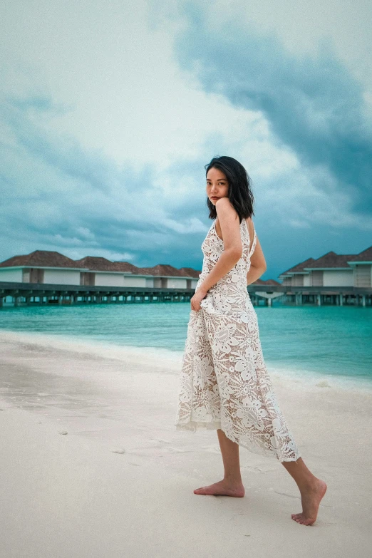 a woman walking across the beach with a cloudy sky behind her