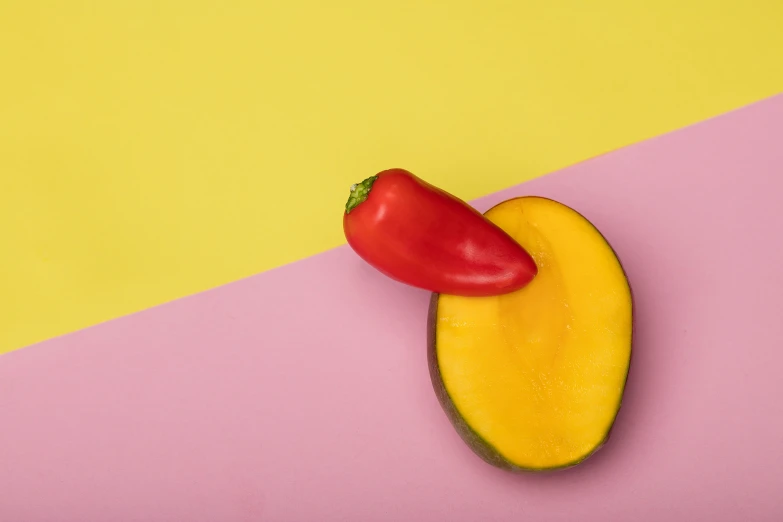 a red pepper, yellow and black pepper on a pink and yellow surface