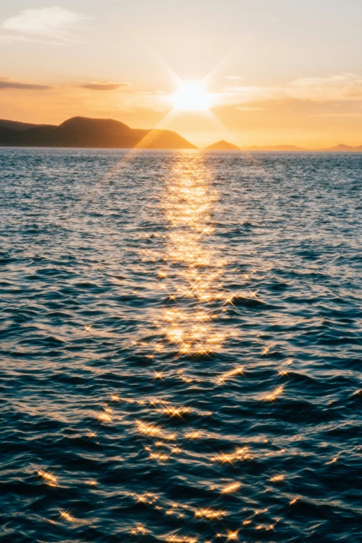 the sun is setting over water with some mountains in the distance