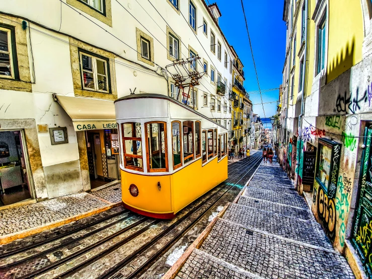 a yellow tram car on tracks running through a narrow street