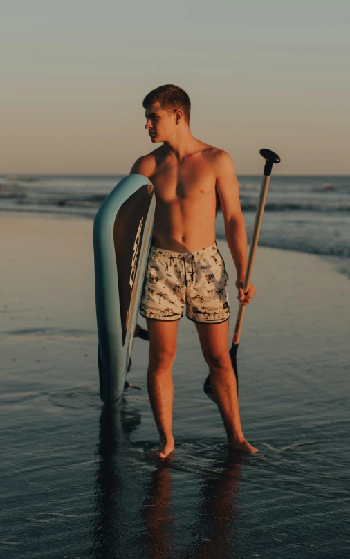 a shirtless man with his surfboard and axe walking along the beach