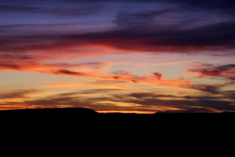 a airplane flies high above the horizon of an almost cloudy sunset