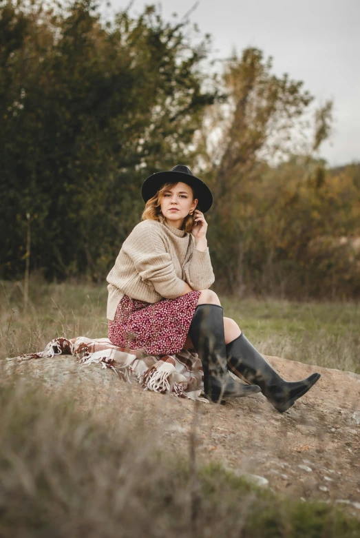 a woman wearing boots and a hat is sitting down