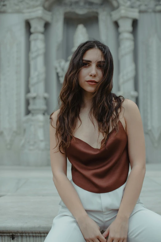 a woman wearing white pants sits and looks off to the side