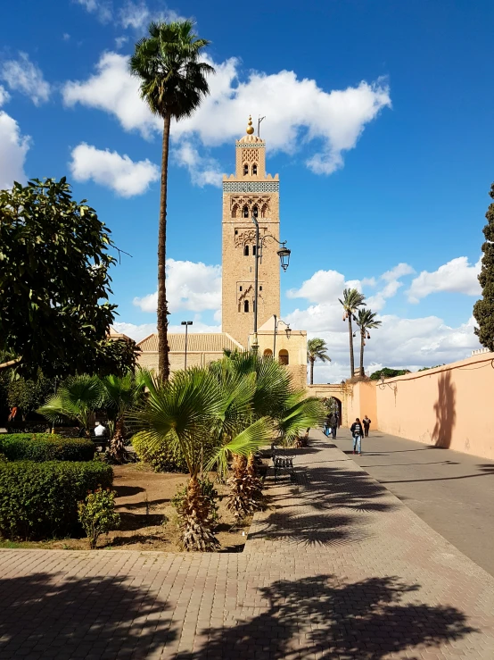 palm trees and people walk near an ancient clock tower