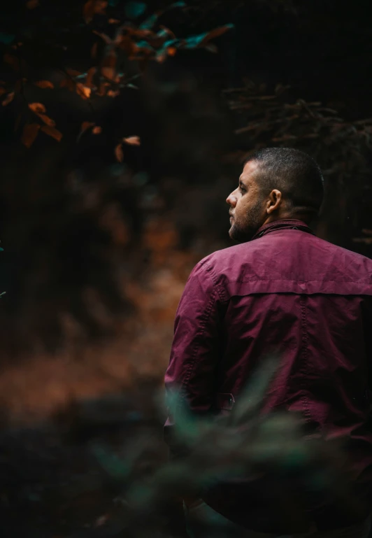 a man in a maroon jacket standing by some trees