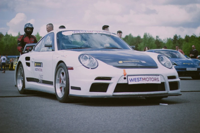 a white sports car with a license plate sits on the road in front of people