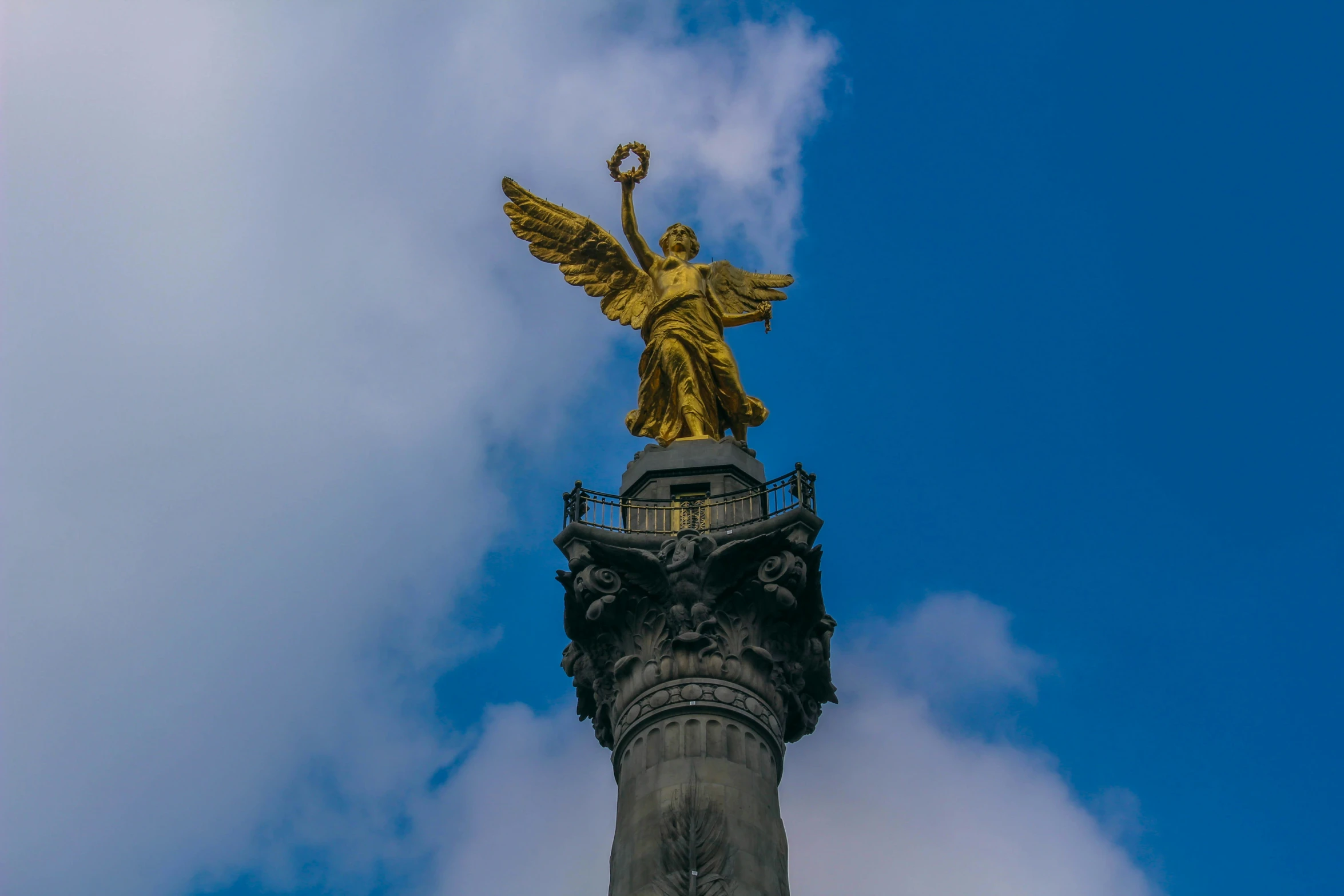 a golden statue atop a metal pillar against a blue cloudy sky