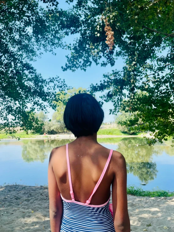 a girl is sitting under some trees looking out at the lake